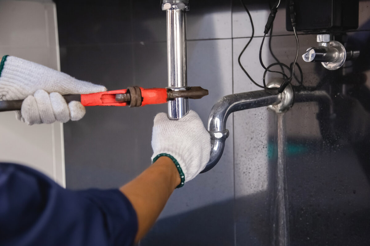 Plumber fixing a plumbing disaster under the sink using an adjustable wrench.