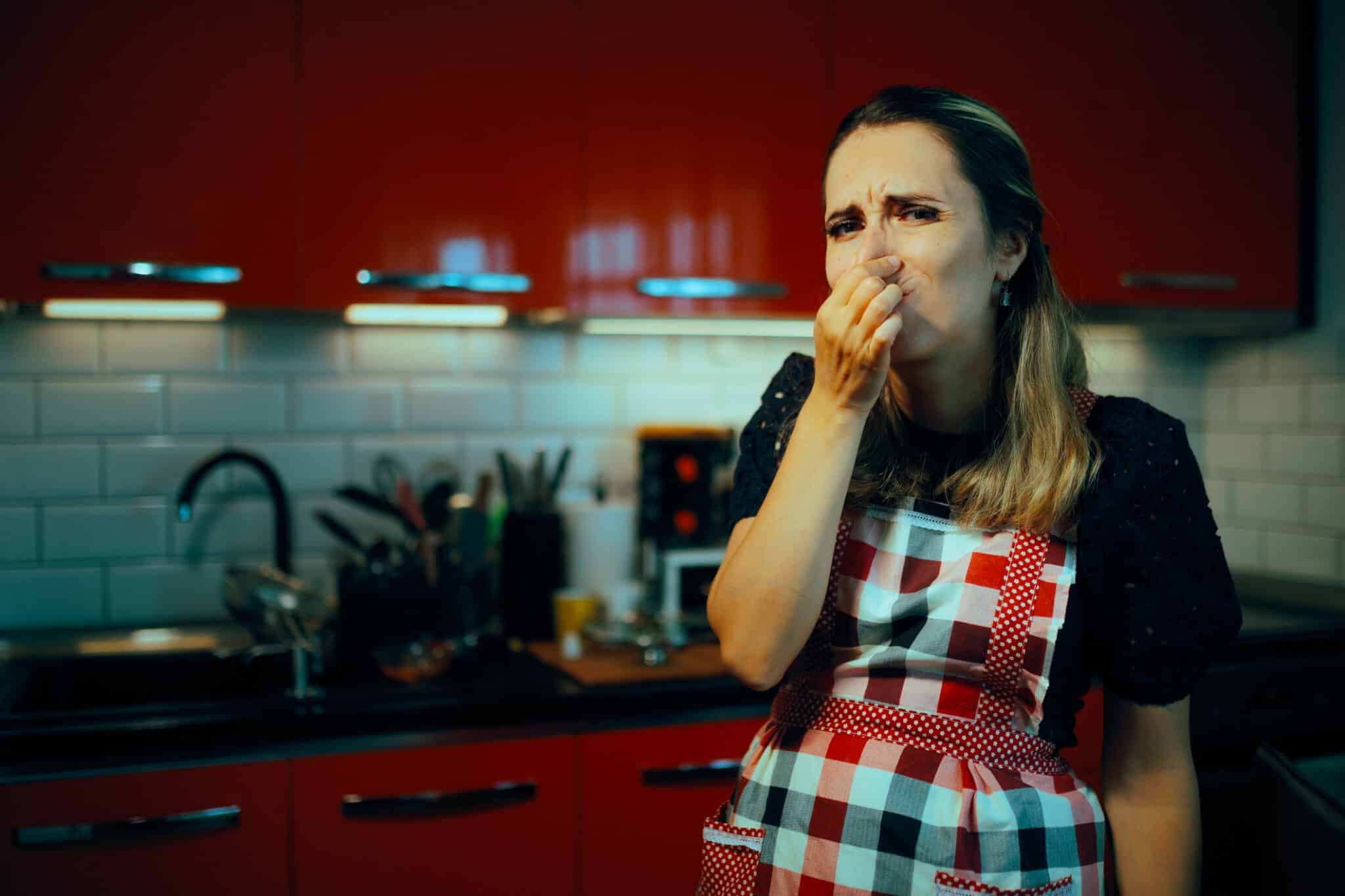 Woman covering her nose, needing drain odor diagnosis in kitchens.
